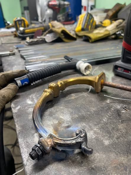 Brass chandelier arm clamped on the bench beside a TIG torch